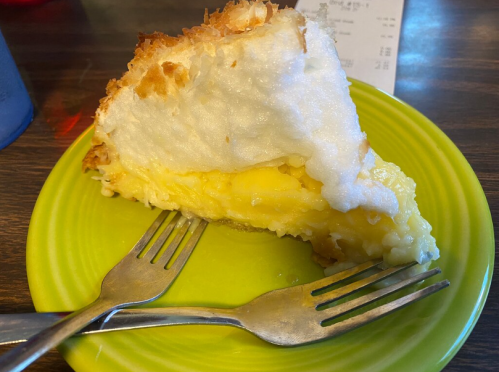 A slice of coconut cream pie on a bright green plate, with two forks beside it.