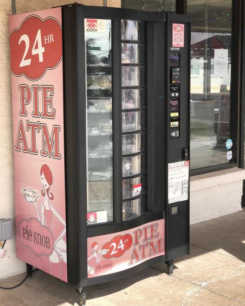 A vending machine labeled "24 HR PIE ATM" with a pink design, offering various pies for sale.
