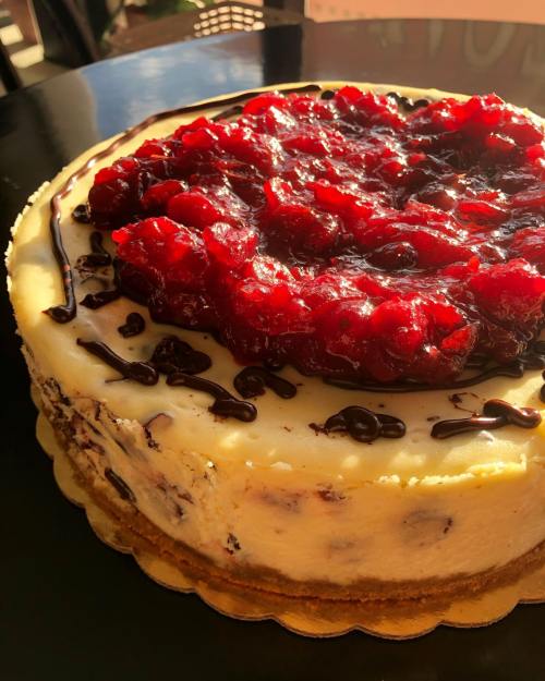 A delicious cheesecake topped with a layer of red fruit compote and drizzled with chocolate sauce.