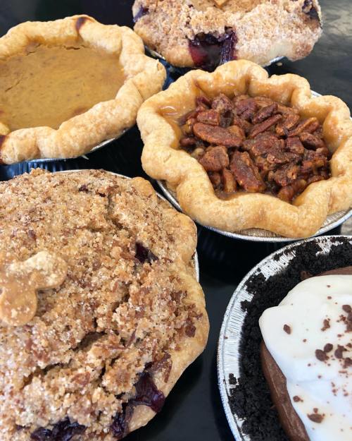 A variety of delicious pies, including pumpkin, pecan, and fruit, arranged on a black surface.