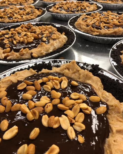 Close-up of multiple chocolate peanut butter pies topped with crushed peanuts in silver pie tins.