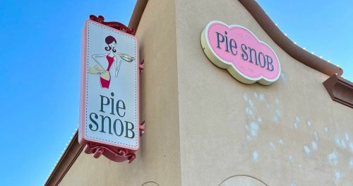 Sign for "Pie Snob" on a building, featuring a cartoon woman holding a pie, with a clear blue sky in the background.