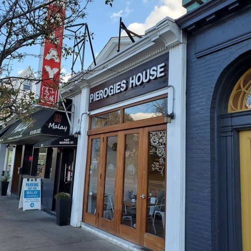 Exterior of Pierogies House restaurant with large windows, next to a sign for Malay, on a sunny day.