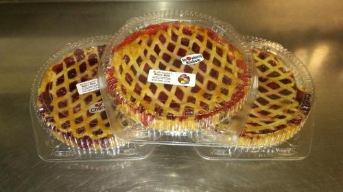 Three fruit pies in clear plastic containers, featuring lattice crusts, labeled cherry and strawberry-rhubarb.