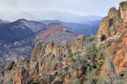 A scenic view of rugged mountains with colorful rock formations and sparse vegetation under a cloudy sky.