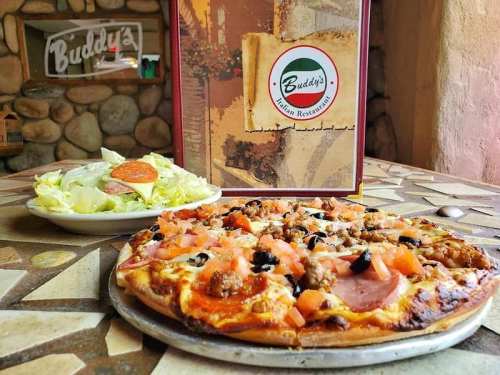 A delicious pizza topped with various ingredients, alongside a fresh salad, on a textured table with a restaurant menu.