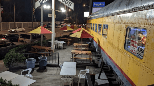 A vintage train car converted into a restaurant with outdoor seating and colorful umbrellas.