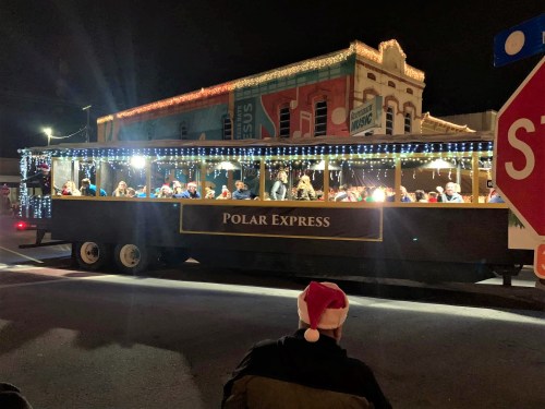 A festive train-like float named "Polar Express" with passengers, decorated with lights, in a nighttime setting.