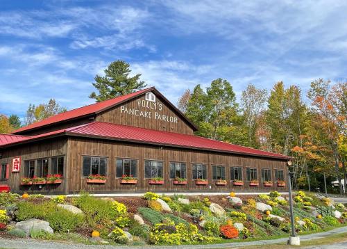 A rustic wooden building with a red roof, labeled "Polly's Pancake Parlor," surrounded by colorful flowers and trees.