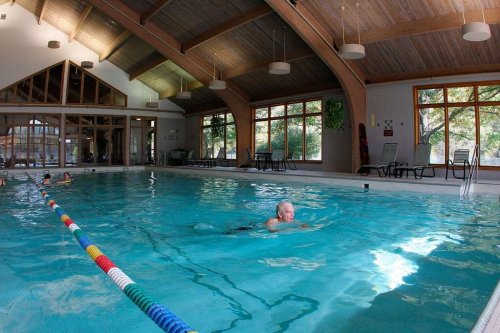 A spacious indoor pool with large windows, featuring swimmers and lounge chairs around the water.