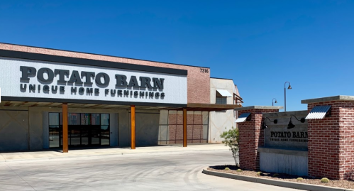 Exterior of a building labeled "Potato Barn" with a sign for unique home furnishings against a clear blue sky.