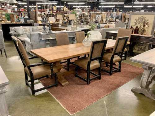 A wooden dining table with four chairs on a rug, surrounded by various home decor items in a store.