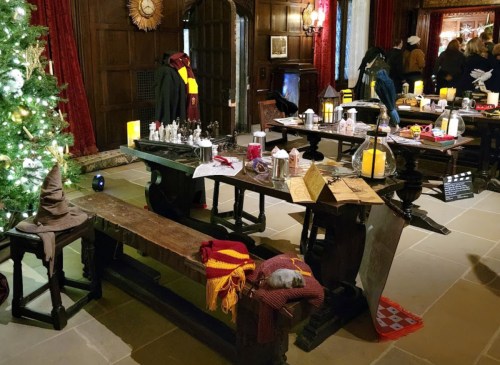 A festive room with a decorated tree, wooden tables, and Hogwarts-themed items, including a sorting hat and candles.