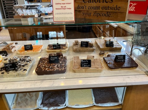 A display case filled with various fudge flavors, each labeled, including chocolate, cookies and cream, and more.
