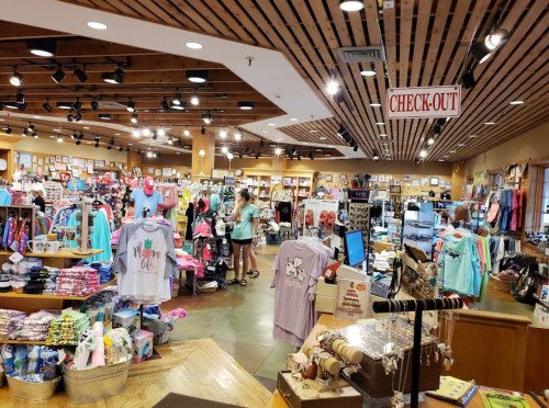A vibrant retail store filled with colorful clothing and merchandise, featuring a checkout area and shoppers browsing.