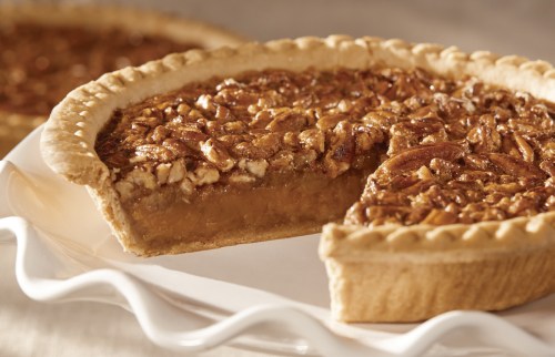 A delicious pecan pie with a slice removed, showcasing its rich filling and flaky crust on a white plate.