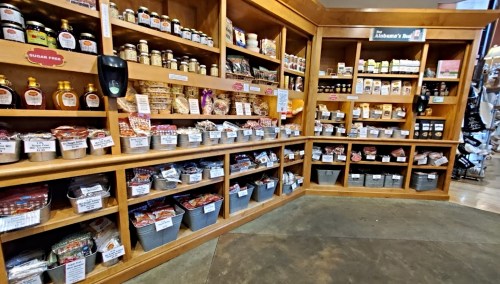 A wooden display of various food items and jars organized on shelves and in bins in a grocery store.