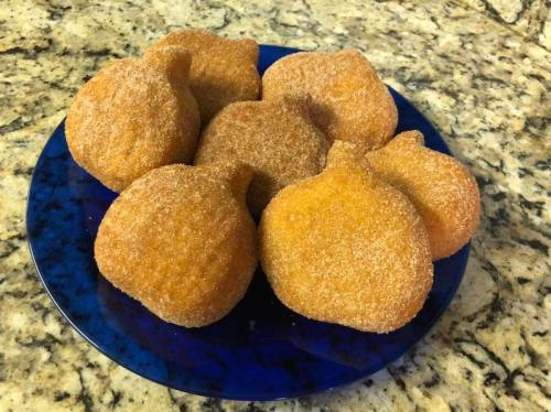 A blue plate holds eight golden-brown, sugar-coated pastries shaped like small pumpkins.