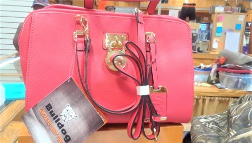 A pink handbag with gold accents and a Bulldog tag displayed on a counter in a store.