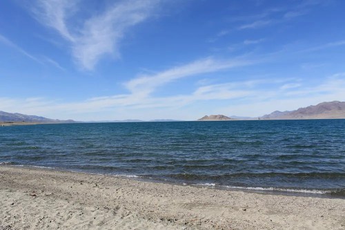 A serene beach scene with gentle waves lapping at the shore under a clear blue sky and distant mountains.