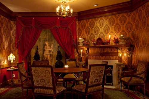 A cozy, elegantly decorated room with a round table, plush chairs, a fireplace, and ornate wallpaper.