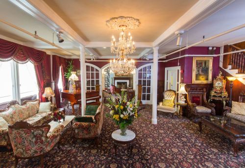 Elegant living room with chandeliers, floral arrangements, vintage furniture, and rich decor in warm colors.