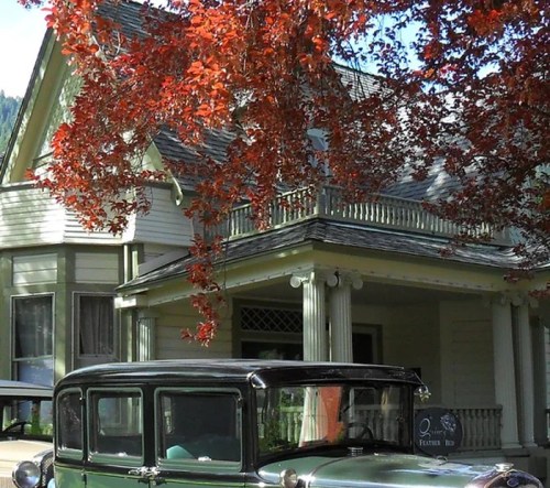 A vintage green car parked in front of a charming house, surrounded by vibrant red autumn leaves.