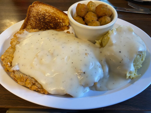 A plate of fried chicken smothered in gravy, mashed potatoes, okra, and a slice of toasted bread.
