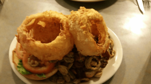 A plate featuring a burger topped with two large, crispy onion rings and garnished with lettuce and tomato.