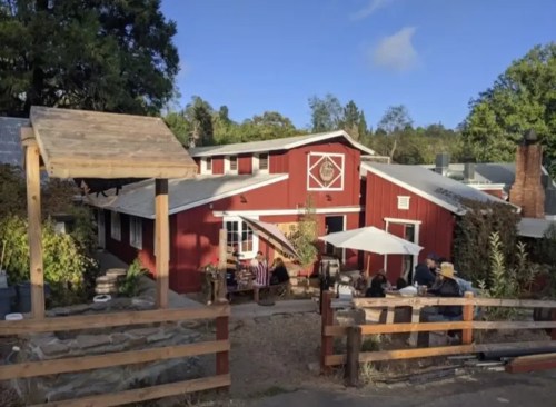 A charming red barn-style building with outdoor seating and a stone pathway, surrounded by greenery and trees.