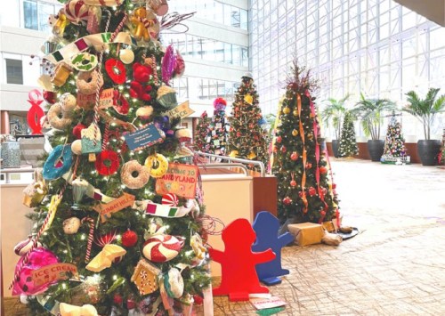 Colorful Christmas trees decorated with playful ornaments and themed displays in a bright indoor space.