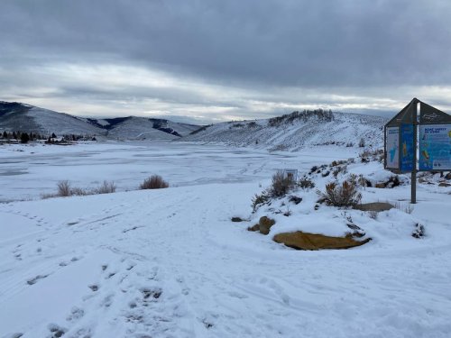 A snowy landscape with a frozen lake, mountains in the background, and an informational sign on the right.