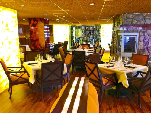 Elegant restaurant interior with wooden floors, stylish chairs, and illuminated walls, featuring tables set for dining.