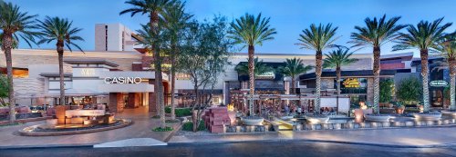 Exterior view of a casino with palm trees, outdoor seating, and a vibrant atmosphere during twilight.