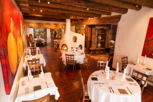 Cozy restaurant interior with wooden beams, colorful artwork, and elegantly set tables. Warm, inviting atmosphere.