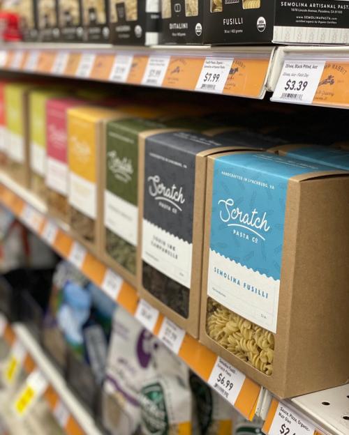 A shelf displaying various boxes of Scratch Pasta Co. semolina pasta in different colors and shapes.