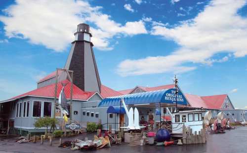 A large building with a lighthouse-style tower, featuring a blue awning and various boats and equipment outside.
