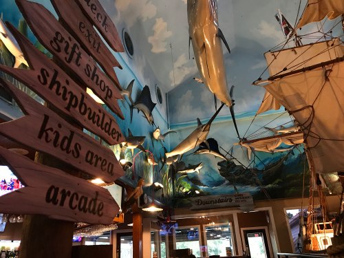 Interior of a themed restaurant featuring a mural of dolphins, a ship, and wooden signs for various attractions.