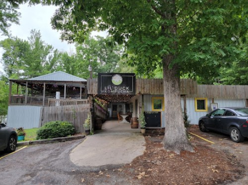 Exterior of Lil Duck Kombucha, featuring a wooden building, outdoor seating area, and surrounding greenery.