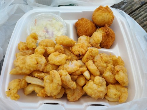 A takeout container filled with fried shrimp, hushpuppies, and a small cup of coleslaw.