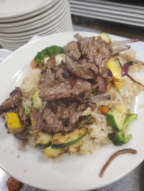 A plate of stir-fried beef over rice, topped with mixed vegetables like zucchini, broccoli, and bell peppers.