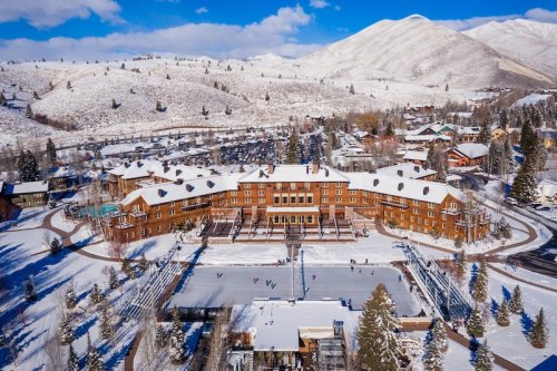 Aerial view of a snow-covered lodge surrounded by mountains and trees, with a frozen rink in the foreground.