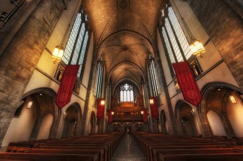 Interior of a grand church with high ceilings, stained glass windows, wooden pews, and decorative banners.