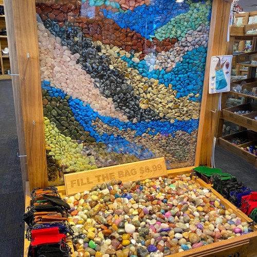 A display of colorful stones arranged in patterns, with a sign reading "FILL THE BAG $6.99" at the bottom.