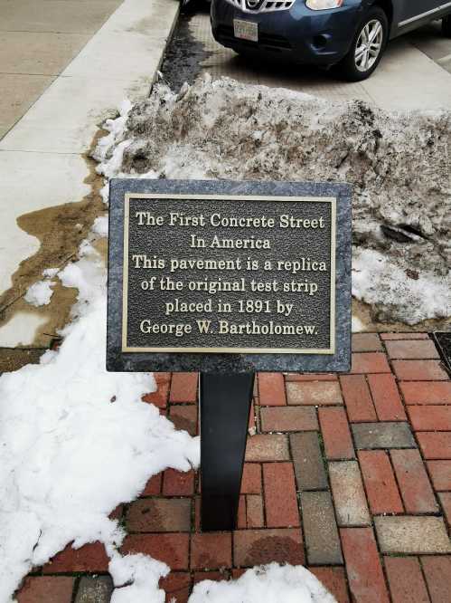 Sign marking the first concrete street in America, detailing its history and the original test strip from 1891.