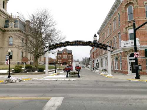 Archway sign over a street reads "Columbus Avenue, 1900, Oldest Concrete Street in America," with historic buildings nearby.