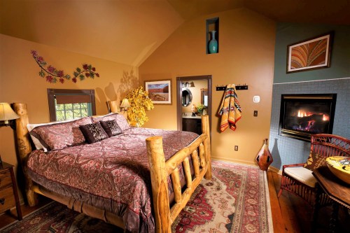 Cozy bedroom with a log bed, warm colors, decorative art, and a fireplace, creating a welcoming atmosphere.