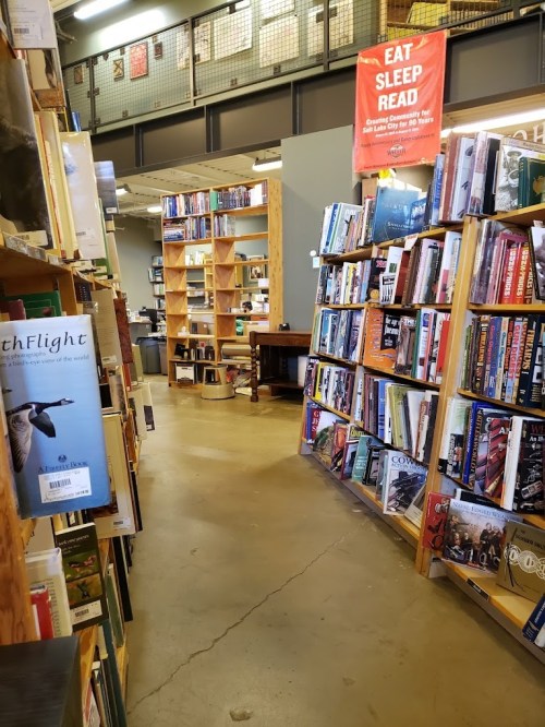 A cozy bookstore aisle lined with bookshelves, leading to a reading area and a "Eat Sleep Read" banner overhead.