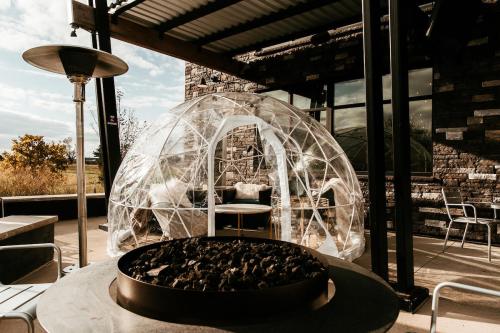 A transparent dome structure with seating inside, next to a circular fire pit on a patio.
