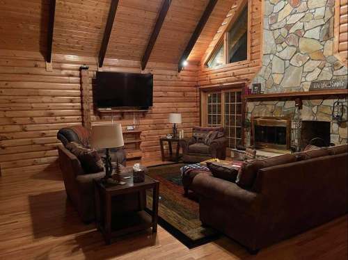 Cozy log cabin living room with wooden beams, stone fireplace, and comfortable seating. Warm, inviting atmosphere.